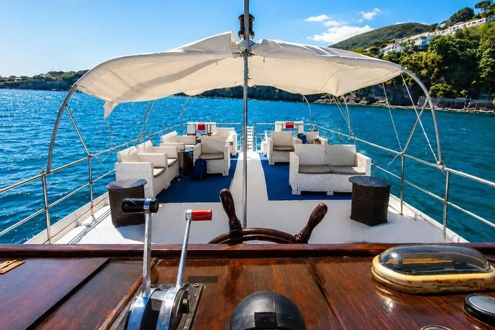 Wooden gozzo boat cruising past the cliffs of Ischia on a boat excursion with lunch on board around Ischia, Campania, Italy